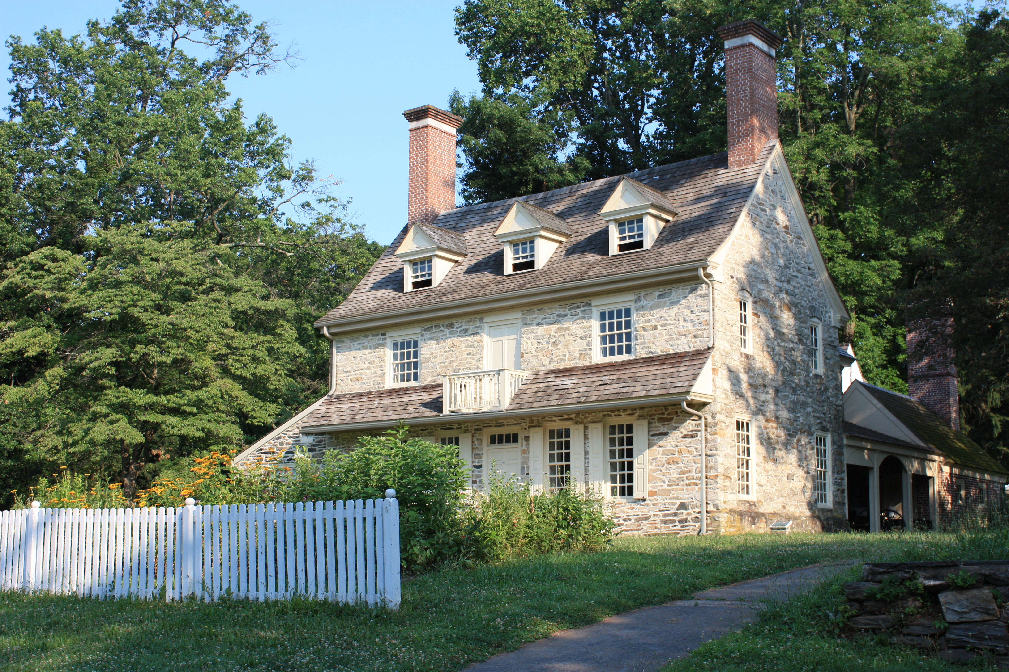 Stone colonial house with white gutters and downspouts, dormer windows, and mature trees